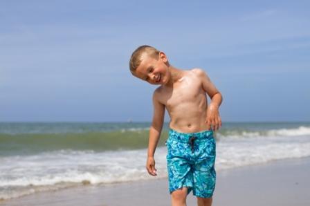 Мальчик на фоне моря наклонил голову, чтобы освободить ухо от воды